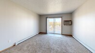 Located at 1802 40th St S in Fargo, North Dakota, this five-bedroom, one-bathroom unit offers a practical and well-organized single-floor layout. The open-concept living and kitchen area forms the heart of the unit, where warm oak cabinetry lines the galley-style kitchen, complemented by white appliances including a range, refrigerator, and dishwasher, along with a stainless steel sink and tile flooring. A pass-through window connects the kitchen to the living area, which features plush carpeting, a textured ceiling, and a sliding glass door that opens onto a private balcony with outdoor views — filling the space with natural light. The spacious living room also includes a wall-mounted air conditioning unit and baseboard heating. Each of the five bedrooms is carpeted and features neutral walls with a textured ceiling, and several rooms include natural light from windows with blinds. The primary bedroom offers a generous closet with sliding doors. A shared full bathroom includes a tub/shower combination, toilet, wood-vanity with a large mirror, and tile flooring. Baseboard heating is present throughout, ensuring consistent comfort. This unit provides abundant bedroom capacity in a functional, straightforward layout suited for shared living.