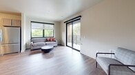 This well-appointed 2-bedroom, 2-bathroom apartment spans 860 square feet on a single floor, offering a thoughtfully designed layout with modern finishes throughout. The open-concept living room features light hardwood flooring, neutral walls, and large windows that fill the space with natural light. A sliding glass door leads to a private balcony with neighborhood views, enhancing the airy ambiance of the living area. The kitchen is a standout feature, equipped with stainless steel appliances including a refrigerator, range, microwave, and dishwasher. Gray cabinetry, white subway tile backsplash, open shelving, and a white quartz peninsula with bar seating create a functional and stylish culinary space. The primary bedroom measures 190 square feet, providing ample space, while both bedrooms feature hardwood-style flooring, large windows with roller shades, and closet storage. Both bathrooms are finished consistently, each offering a tub/shower combo, gray vanity with white countertop, chrome fixtures, and hardwood-style flooring. The unit's clean, contemporary aesthetic and practical design make it a comfortable and inviting living space.