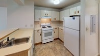 This single-story residence offers a well-organized layout with a generous open living area at its core. The living room is carpeted and bathed in natural light through a full-width sliding glass door fitted with vertical blinds, providing direct outdoor views and patio access. The space flows naturally toward a kitchen separated by a breakfast bar counter. The kitchen is equipped with white cabinetry featuring wood-tone hardware, a gas range, refrigerator, built-in range hood, and a double sink, all set atop durable tile flooring.

Multiple bedrooms are finished with neutral wall-to-wall carpeting. The primary bedroom features a walk-in closet and a wide window overlooking the exterior. A second bedroom offers ample space and natural light through slatted blinds. Both bathrooms are finished with tile flooring and include a tub-shower combination, toilet, and vanity with built-in cabinetry and mirrored storage. A dedicated laundry room houses full-sized washer and dryer units on tile flooring with overhead shelving. Throughout, the space maintains a clean, neutral palette with consistent finishes.