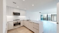 This contemporary two-floor space is defined by clean lines, a neutral palette, and an abundance of natural light. The open-plan kitchen and living area forms the heart of the main floor, where light wood flooring flows seamlessly throughout. The kitchen is outfitted with flat-front cabinetry in a warm off-white finish, stainless steel appliances including a gas cooktop, wall oven, and built-in microwave, complemented by granite countertops and a subway tile backsplash. The living area extends toward large floor-to-ceiling sliding glass doors that open to an outdoor balcony, inviting ample natural light and outdoor views. A second room on this level also benefits from direct balcony access via its own set of glass sliding doors. The bathrooms are finished to a high standard, featuring marble-tiled walls and floors, a glass-enclosed walk-in shower, and vanities with granite countertops. A half bath provides added convenience. The upper floor offers additional living space bathed in sunlight, with a staircase connecting the two levels. Recessed lighting throughout and a consistent use of light tones create a bright, airy ambiance across the entire space.