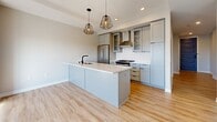 Located in Edina, Minnesota, this single-floor residence at 4999 Halifax Ave S showcases a thoughtfully designed interior with modern finishes and a clean, cohesive aesthetic. The kitchen serves as a focal point of the space, featuring gray shaker-style cabinetry with matte black hardware, white quartz countertops, a classic subway tile backsplash, stainless steel appliances, and a stainless range hood. A large center island with an integrated sink is illuminated by striking geometric pendant lights, creating both functional workspace and a stylish gathering area. Light-toned hardwood flooring flows throughout the main living and kitchen areas, adding warmth to the neutral color palette. The bedrooms are bright and well-proportioned, with large black-framed windows that invite abundant natural light and offer elevated views of the surrounding Edina neighborhood. Carpeted flooring in the bedrooms provides comfort underfoot. The bathroom is finished with marble-look tile flooring, a gray vanity with ample drawer storage, a white quartz countertop, an undermount sink, and matte black fixtures, lending a refined, contemporary feel. The overall ambiance of the space is clean, modern, and move-in ready, with consistent design choices that create a polished and cohesive living environment throughout.