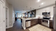 This well-appointed single-floor residence offers a thoughtfully designed open-concept layout that seamlessly connects the kitchen, dining, and living areas. The kitchen is a standout feature, equipped with stainless steel appliances including a range, microwave, and dishwasher, complemented by a two-tone cabinet scheme pairing dark espresso lower cabinets with crisp white upper cabinets. Granite countertops extend across the surfaces and onto the kitchen island, which is illuminated by a series of stylish pendant lights. A subway tile backsplash adds a refined touch throughout. Dark hardwood flooring runs through the main living areas, anchoring the open-concept space. The living room features an accent wall with textured wallcovering, large windows that invite generous natural light, and a ceiling fan overhead. Two bedrooms are present, each with large windows offering outdoor views. One bedroom features a textured accent wall, while the other showcases bold, dark-painted walls for contrast. A spacious walk-in closet with wire shelving and built-in hanging rods provides ample storage. The bathroom is finished with large-format tile flooring, a granite vanity with dark cabinetry, and a glass-enclosed shower, offering a clean and functional design throughout.