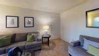 This single-floor residence offers a thoughtfully organized layout across several distinct living areas. The living room provides a comfortable, carpeted space with neutral tones, ceiling fan, and an entry door, creating a welcoming atmosphere. Adjacent to it, a dedicated dining nook accommodates a full dining set and is finished with tile flooring and a ceiling fan overhead.

The galley-style kitchen is efficiently designed with rich dark wood cabinetry extending to the ceiling, providing generous storage. It features a double stainless steel sink, laminate countertops, tile flooring, and white appliances including a range and dishwasher, with a utility closet accessible at the rear.

The primary bedroom is a carpeted retreat with a ceiling fan, a window with blinds for natural light, and ample wall space. It connects to a hallway featuring a vanity with a single sink, dark wood cabinetry, a large lighted mirror, and access to a separate water closet. A second bedroom, also carpeted, offers a closet with bifold doors and its own mirror accent, making it suitable as a guest room or secondary sleeping space.

Throughout the residence, textured walls, consistent neutral paint, and tile-to-carpet transitions contribute to a cohesive and functional interior aesthetic.