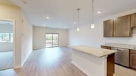 Located at 903 Main Street in Mukwonago, Wisconsin, this well-appointed one-bedroom unit offers a thoughtfully designed layout across a single floor. The open-concept living and kitchen area is bright and airy, featuring light-toned luxury vinyl plank flooring, recessed lighting, and a neutral color palette throughout. The kitchen is a standout feature, equipped with rich dark-wood cabinetry, granite countertops, a breakfast bar with pendant lighting, and a full suite of stainless steel appliances including a range, microwave, and refrigerator. A sliding glass door in the living area opens to a private balcony with views of the surrounding Mukwonago streetscape and green spaces. The generously sized primary bedroom is finished with plush carpeting, a large window that brings in natural light, and access to two closets, including a walk-in closet with built-in shelving and hanging rods. Additional practical features include an in-unit laundry area. Clean lines, modern finishes, and a functional floor plan make this unit a comfortable and stylish living space in a convenient Main Street location.