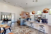 Located at 1312 Smither Dr in Huntsville, Texas, this single-story community clubhouse delivers a contemporary design across a generously sized floor plan. The welcoming leasing area greets visitors with striking copper globe pendant lights, a textured accent wall, polished concrete floors with bold hexagonal inlay patterns, and a sleek service counter with bar-height seating. Floor-to-ceiling glass doors flood the entry with natural light and offer views of the surrounding greenery.

The two living areas serve distinct purposes. The main lounge features soaring ceilings, multiple skylights, a vibrant teal accent wall, mounted flat-screen television, and comfortable seating arrangements ideal for gathering. A second lounge — accessed through frosted glass double doors — offers a game room with a full-size pool table, additional lounge seating, and decorative signage.

A dedicated study room provides an abundance of natural light through tall windows overlooking the trees, vivid blue carpeting, round work tables, and a dramatic sputnik chandelier. An additional bar lounge area features a large communal high-top table, a wet bar with stainless steel countertops, a wall-mounted television, bold red hexagonal wallpaper, and a striking equestrian art piece. Vending machines and access to adjacent amenity spaces round out this well-appointed clubhouse.
