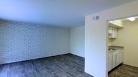 This single-floor space offers a compelling blend of industrial character and modern simplicity. The most striking architectural feature is the painted white exposed brick wall, which runs the length of the main room and adds rich texture and visual depth to the interior. The contrast between the raw, tactile brickwork and the smooth white ceiling creates a refined yet approachable ambiance.

The flooring throughout is a dark hardwood-style material, lending warmth and a grounded, contemporary feel to the space. The dark tones of the floor play beautifully against the bright white surfaces of the walls and ceiling, creating a well-balanced visual composition.

The room is characterized by clean lines and an open layout, giving the space a versatile, uncluttered feel that lends itself well to a variety of uses. A ceiling-mounted HVAC vent is integrated into the design, ensuring climate comfort while maintaining the clean aesthetic. The smooth drywall surfaces on the adjacent walls provide a neutral backdrop that complements the bold brick accent.

Overall, this space carries a modern industrial character, with its exposed brick, dark flooring, and crisp white finishes combining to create an interior that feels both stylish and functional.