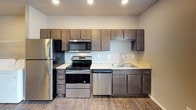 This single-floor unit offers a practical and well-appointed layout designed for comfortable everyday living. The kitchen serves as a functional centerpiece, featuring dark espresso-toned cabinetry, light countertops, and a full suite of stainless steel appliances including a refrigerator, electric range, built-in microwave, and dishwasher. Recessed lighting illuminates the space, and durable wood-look flooring runs throughout, providing a cohesive aesthetic across the unit.

A dedicated laundry area is conveniently located adjacent to the kitchen, housing a full-sized washer and dryer alongside wire shelving for additional storage. The living area is open and versatile, offering neutral wall tones, a ceiling light fixture, and a wall-mounted HVAC unit beneath a window that brings in natural light.

A secondary open room features wood-look flooring and connects to a carpeted hallway, offering flexible use as a bedroom or additional living space. The walk-in closet is accessed through a paneled door and includes wire shelving with a hanging rod for organized storage. The bathroom is outfitted with a clean, all-white tub and shower surround. Throughout the unit, neutral tones and consistent flooring create a cohesive, move-in-ready environment.