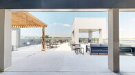 The Sky Lounge at 3751 Heritage Towne Blvd in Midlothian, Texas is a generously sized rooftop balcony destination designed for outdoor gathering and relaxation. The space blends modern architectural elements with warm natural accents, most notably a striking wood-beam pergola that provides partial shade over an open-air dining area outfitted with multiple seating arrangements. A contemporary covered pavilion with recessed lighting and clean concrete columns anchors one section of the terrace, offering a sheltered lounge area furnished with plush, cushioned seating ideal for conversation and unwinding. An additional covered corner balcony features sleek horizontal black railings and recessed ceiling lights, framing sweeping views of the surrounding Midlothian landscape and open skies. The outdoor kitchen counter area along the perimeter adds a functional amenity for entertaining. Throughout the rooftop, light-toned concrete flooring reflects natural sunlight, contributing to the bright, airy atmosphere. The design balances open and covered zones seamlessly, accommodating both sun-seekers and those preferring shade. With panoramic views extending across the Texas horizon, the Sky Lounge offers an elevated communal experience that is both inviting and visually striking year-round.
