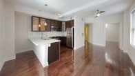 Situated at 145 Granby Street in the heart of Norfolk, Virginia, this single-floor residence offers a thoughtfully designed interior that balances modern finishes with everyday functionality. The open-concept kitchen is a standout feature, showcasing rich dark espresso cabinetry with glass-front upper cabinets, sleek white stone countertops, and a full suite of stainless steel appliances including a range, microwave, dishwasher, and refrigerator. A white subway tile backsplash adds a clean, contemporary touch, while elegant pendant lighting illuminates the kitchen peninsula. Rich, dark hardwood flooring flows seamlessly throughout the main living areas, adding warmth and continuity to the space. The living area is generously proportioned with a ceiling fan and an open connection to the kitchen, creating an inviting and airy atmosphere. The bedroom features the same hardwood flooring, neutral walls, and a window fitted with blinds that allows for natural light. The bathroom is finished with light-toned tile flooring and wall surround, offering a bright and clean aesthetic with a tub-shower combination. Overall, the unit presents a polished, move-in-ready environment with cohesive design elements throughout.