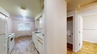 Located at 8660 N Columbia Blvd in Portland, Oregon, this one-bedroom, one-bathroom unit offers a practical and comfortable single-floor layout. The combined kitchen and dining area is equipped with white cabinetry, a dishwasher, electric range, and a single-basin sink, all set on wood-style laminate flooring that extends through the common areas. A window in the kitchen brings in natural light and overlooks the surrounding greenery. The open living room transitions seamlessly from carpet to the laminate floor of the kitchen, and features a sliding glass door that opens onto a private balcony with views of the landscaped community grounds and neighboring buildings. The bedroom is carpeted and comfortably sized, featuring a dedicated closet with built-in shelving and hanging rods, and a window with blinds that allows natural light in. Two additional closets provide generous storage throughout the unit. The bathroom includes a vanity with a large mirror, a single-sink countertop, and wood-style flooring. Baseboard heating is present throughout the unit, ensuring year-round comfort. Neutral tones and clean finishes create a bright, move-in ready environment.