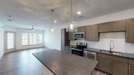 This single-floor residence on Mannington Drive in Greensboro, NC, showcases a contemporary design with an open-concept layout that seamlessly connects the kitchen and living areas. The kitchen is a standout feature, outfitted with taupe shaker-style cabinetry, dark granite countertops, and a full suite of stainless steel appliances, including a range, microwave, dishwasher, and refrigerator. A white subway tile backsplash adds a clean, modern contrast, while a central island with matching granite provides additional prep and dining space. Pendant lighting with clear glass globe fixtures hangs above the island, complementing the recessed lighting throughout. Wood-look plank flooring extends across the kitchen and living areas, adding warmth and continuity. The living room is bright and open, benefiting from large windows that invite abundant natural light, a ceiling fan, and direct access to an outdoor area. The bedroom features plush carpeting, a ceiling fan, and a well-sized window. The bathroom includes a tub-shower combo with tiled surround, granite-topped vanity with taupe cabinetry, and tile flooring, maintaining the cohesive, modern aesthetic found throughout the space.