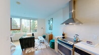 Located at 855 NE Multnomah St in Portland's Lloyd District, this efficiently designed studio offers a thoughtfully arranged single-floor layout that maximizes every square foot. A welcoming entrance leads down a light-filled corridor into the open-concept main living area, where light hardwood flooring and soft neutral walls create a clean, modern aesthetic throughout.

The kitchen is a standout feature, outfitted with stainless steel appliances including a GE electric range with a sleek overhead ventilation hood, a built-in dishwasher, and a full-size refrigerator. Light wood cabinetry, white quartz countertops, a subway tile backsplash, and a stainless steel sink complete this well-appointed cooking space. Upper cabinetry provides additional storage, along with a built-in microwave.

The open living and sleeping area benefits from a large picture window that frames lush outdoor greenery and neighboring building views, flooding the space with natural light. The layout comfortably accommodates both a living and sleeping arrangement within one cohesive room.

The bathroom/laundry combination is clean and functional, featuring matching light wood cabinetry, a large vanity mirror, and consistent hardwood-style flooring. A dedicated closet offers practical storage. The overall ambiance is contemporary and efficient, ideal for modern urban living in the heart of Portland.