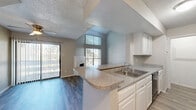 This two-story home offers a thoughtfully organized layout across two floors, with the main living areas on the ground floor and bedrooms above. The living room is a standout space, featuring soaring vaulted ceilings, a tile-surround fireplace, and tall windows that draw in abundant natural light. Wood-look flooring runs throughout the main level, adding warmth and continuity to the open feel. The kitchen flows seamlessly into the living area via a peninsula with granite-style countertops, a double sink, and ample white cabinetry. A dedicated pantry and hallway provide additional storage and connectivity on the lower level. Upstairs, the primary bedroom is generously sized with carpeted flooring, natural light from dual windows, and access to a closet. The second bedroom, also carpeted, features a large window and its own closet. Both bathrooms are finished with white cabinetry, granite-style countertops, and wood-look tile flooring. The primary bath includes a wide vanity with dual mirrors and a soaking tub. A carpeted staircase with a white railing connects the two floors. Textured ceilings are present throughout, complementing the home's clean, neutral palette.