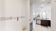 This thoughtfully designed single-floor unit in Weatherford, Texas, maximizes every inch of its compact footprint with a clean, modern aesthetic. Light wood-tone flooring flows throughout, complemented by crisp white walls and recessed lighting that keeps the space feeling bright and open.

The kitchen is a standout feature, showcasing rich dark-wood cabinetry, stainless steel appliances, and a sleek white quartz peninsula with bar seating illuminated by pendant lights — ideal for casual dining or entertaining. A built-in wine cooler adds a refined touch near the entryway, which also includes a practical wall-mounted coat hook rail and open shelving.

The living room benefits from large windows dressed with floor-length curtains, inviting generous natural light and offering pleasant outdoor views of the surrounding greenery. The space comfortably accommodates a seating area with a warm, contemporary feel.

The bathroom is elegantly appointed with dark wood vanity cabinetry, granite countertops, a wide mirror with overhead lighting, and a tiled walk-in shower, offering a spa-like atmosphere. It connects directly to the sleeping area, which features the same light flooring and recessed lighting for a cohesive, tranquil environment.

A dedicated closet provides organized storage, rounding out this well-appointed and efficiently planned modern unit.