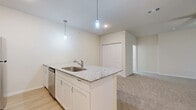 This single-floor residence offers a practical and modern layout across two bedrooms and two full bathrooms. The open-concept kitchen serves as the heart of the home, showcasing granite countertop surfaces, crisp white cabinetry, a stainless steel appliance suite including a range, microwave, refrigerator, and dishwasher, and a peninsula island with a built-in sink. Pendant lighting above the island adds a stylish touch, while light wood-look flooring grounds the kitchen and dining area with warmth.

The living area extends naturally from the kitchen, featuring plush carpeting, a ceiling fan, and vertical blinds that filter natural light. The primary bedroom is a comfortable retreat with carpet flooring, a ceiling fan, a window with blinds, and access to a closet. The second bedroom mirrors the same neutral, carpeted aesthetic and connects conveniently to the rest of the unit.

Both bathrooms are finished consistently with granite vanity tops, white shaker-style cabinetry, wood-look tile flooring, and tiled shower-tub combinations. The clean, neutral color palette of warm beige walls and white trim runs throughout the entire space, creating a cohesive and move-in-ready environment.