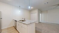 This single-floor residence offers a practical and modern layout across two bedrooms and two full bathrooms. The open-concept kitchen serves as the heart of the home, showcasing granite countertop surfaces, crisp white cabinetry, a stainless steel appliance suite including a range, microwave, refrigerator, and dishwasher, and a peninsula island with a built-in sink. Pendant lighting above the island adds a stylish touch, while light wood-look flooring grounds the kitchen and dining area with warmth.

The living area extends naturally from the kitchen, featuring plush carpeting, a ceiling fan, and vertical blinds that filter natural light. The primary bedroom is a comfortable retreat with carpet flooring, a ceiling fan, a window with blinds, and access to a closet. The second bedroom mirrors the same neutral, carpeted aesthetic and connects conveniently to the rest of the unit.

Both bathrooms are finished consistently with granite vanity tops, white shaker-style cabinetry, wood-look tile flooring, and tiled shower-tub combinations. The clean, neutral color palette of warm beige walls and white trim runs throughout the entire space, creating a cohesive and move-in-ready environment.