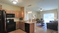 Located at 850 Lisburn Rd in Camp Hill, Pennsylvania, this single-floor residence offers a well-designed open-concept layout that seamlessly connects the kitchen and living areas. The kitchen is appointed with warm honey-toned cabinetry, granite countertops, and a peninsula island that provides additional prep space and casual seating. Black appliances, including a range, microwave, and dishwasher, complement the cabinetry, while pendant lighting above the island adds a refined decorative touch. Light-toned hardwood-style flooring runs throughout, creating a cohesive and clean aesthetic. The adjacent living area is bright and airy, benefiting from large windows and a sliding glass door that invites natural light and outdoor access. A ceiling fan keeps the space comfortable year-round. The neutral wall tones throughout create a versatile backdrop, and the open sightlines between the kitchen and living space make the overall floor plan feel expansive and connected. This residence combines functional design with comfortable living in a single, thoughtfully laid-out floor.