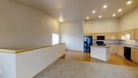 This single-floor residential unit offers a functional and well-organized layout designed for comfortable everyday living. The open-concept main living and kitchen area is a standout feature, boasting soaring vaulted ceilings that lend an airy, expansive feel to the space. The kitchen is equipped with light wood cabinetry, granite-style countertops, a built-in kitchen island, and black appliances including a refrigerator with an ice and water dispenser, a microwave, and a range. Recessed lighting illuminates the kitchen area, while a window allows natural light to brighten the adjacent living space, which features warm hard-surface flooring. A railed transition separates the carpeted area from the hard-floor kitchen zone, adding a subtle architectural detail. The bedroom is generously sized with soft carpeting underfoot and neutral wall tones throughout. It features two closets — one a sliding mirrored-door style and the other a standard hinged door — providing ample storage. A connected en-suite bathroom is accessible directly from the bedroom and includes tile flooring and a bathtub-shower combination. The unit maintains a clean, neutral palette throughout, with white trim and subdued tones creating a cohesive and move-in-ready atmosphere.