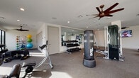 This single-level fitness center is thoughtfully designed to support a wide range of workout styles and training goals. The space is divided into several functional zones, each outfitted with dedicated equipment to maximize versatility and usability.

The cardio area features multiple treadmills, elliptical machines, and StairMaster units positioned along floor-to-ceiling windows that flood the room with natural light and offer views of the surrounding outdoor landscape. Overhead ceiling fans provide comfortable airflow throughout the space.

The strength and free weights zone is anchored by a full rack of dumbbells reflected in a large wall-mounted mirror, creating a sense of depth and openness. A cable machine and functional trainer offer additional resistance training options, while an ab bench and a freestanding BOX heavy bag support core and combat conditioning workouts.

A dedicated functional training area includes kettlebell racks, resistance bands, medicine balls, a wall-mounted mat, and a large tractor tire for high-intensity training. This zone is also bathed in natural light through oversized windows.

Throughout the facility, the design aesthetic is clean and contemporary, with white walls, recessed lighting, and durable rubber flooring. The combination of ample equipment variety, natural light, and thoughtful layout makes this fitness center a comprehensive and inviting training environment.