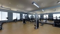 Located at 2200 Bellamy Ct in Greenville, NC, this fitness center offers a well-equipped, single-floor workout facility designed to support a comprehensive exercise experience. The space is finished with durable cork-style flooring, ideal for high-traffic athletic use, and features a neutral color palette of cool grays and muted blues that contributes to a focused, professional atmosphere. Recessed lighting is complemented by suspended linear fixtures and ceiling fans, ensuring the space remains bright and comfortable throughout workouts. Full-length mirrors line the walls, visually expanding the room while allowing users to monitor their form during exercise. The facility is outfitted with a robust selection of strength training machines, including cable systems and multi-use weight stations, as well as benches and various resistance equipment. Large windows allow natural light to filter into the space, enhancing the open, airy feel of the interior. The layout is thoughtfully organized to provide ample room between equipment, promoting safe and efficient movement throughout the floor. Overall, this fitness center combines functionality with a clean, modern aesthetic to deliver an inviting environment for all levels of fitness enthusiasts.