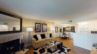 This thoughtfully designed single-floor residence offers a cohesive and functional layout that flows seamlessly from room to room. The living area serves as the heart of the home, anchored by a classic white-tiled fireplace topped with a large framed mirror that reflects natural light pouring in through sliding glass doors leading to an outdoor patio. Wood-style flooring runs throughout, complementing the warm, neutral tones of the walls and textured ceilings.

Adjacent to the living area, the dining space is defined by an elegant chandelier overhead and tasteful wall art, creating an intimate setting for gatherings. The galley-style kitchen is bright and highly functional, featuring crisp white cabinetry, white countertops, recessed lighting, and ample storage on both sides, with a passthrough that maintains a visual connection to the living areas.

The bedroom is a calm retreat, offering natural light through a window dressed with layered curtains and direct access to a well-organized bathroom featuring a white vanity, a large mirror with overhead lighting, and a separate tub-shower combination. A second full bathroom provides additional convenience. Throughout the space, consistent finishes and a clean, neutral palette create a welcoming and versatile living environment.