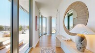 Located at 3401 S La Cienega Blvd in Los Angeles, this thoughtfully designed 3-bedroom, 2-bathroom residence offers a compelling blend of modern architecture and elevated urban living. The open-concept living and dining area is defined by dramatic floor-to-ceiling glass walls that frame sweeping panoramic views of the Los Angeles hillsides and cityscape, flooding the interiors with abundant natural light. Warm hardwood flooring flows throughout, complementing the clean white walls and contemporary aesthetic. A distinctive curved concrete column anchors the dining area, adding an architectural focal point to the space. The living room features built-in cabinetry and generous proportions ideal for entertaining. The outdoor terrace extends the living space further, offering a furnished lounge area with unobstructed open-sky views — perfect for enjoying the Southern California climate. The primary bedroom is comfortably scaled, while the two bathrooms are finished with warm wood vanities, illuminated mirrors, and striking gold-and-white checkered tile flooring. The full bath includes a soaking tub with wall-to-wall square tile surround. A hallway with clean white panel doors and dedicated closet storage rounds out this well-appointed residence.