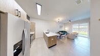 This well-designed single-floor residence offers a thoughtfully arranged open-concept layout encompassing a combined kitchen, dining, and living area, along with one bedroom and one bathroom. The kitchen is a standout feature, showcasing light wood cabinetry with matte black hardware, a white quartz island with a built-in sink and bar seating, stainless steel appliances including a French door refrigerator and electric range, and a skylight overhead that floods the space with natural light. The living area is bright and welcoming, with large sliding glass doors that open to an outdoor green space, a ceiling fan, and ample room for comfortable seating arrangements. The bedroom is calm and neutral, finished with tile flooring, a ceiling fan, and natural light from a window with a roller shade. The bathroom features a striking geometric patterned tile floor, a wood vanity with white countertop, matte black fixtures, a frameless glass walk-in shower, and globe pendant lighting. Throughout the residence, large-format light tile flooring, crisp white walls, and clean modern finishes create a cohesive, contemporary aesthetic that is both functional and visually appealing.