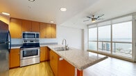 Located at 1455 Kettner Boulevard in San Diego's vibrant Little Italy neighborhood, this 1-bedroom, 1-bathroom unit offers a well-designed layout across a single floor. The open-concept living, dining, and kitchen area forms the heart of the home, featuring light wood-style flooring, recessed lighting, and a ceiling fan. The kitchen is equipped with warm-toned cabinetry, granite countertops, stainless steel appliances including a double oven and microwave, and a peninsula island with a sink — ideal for both cooking and casual dining. Floor-to-ceiling windows flood the living area with natural light and provide access to a private balcony with sweeping views of the San Diego skyline and bay. A bright hallway connects the living area to the private bedroom, which features plush carpeting, a mirrored sliding closet, and a serene atmosphere. The unit includes three closets in total, offering ample storage throughout. The bathroom is finished with granite countertops, warm wood cabinetry, a mirrored medicine cabinet, and tile flooring. A utility room rounds out the layout, adding everyday functionality to this efficiently designed urban residence.