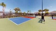 Located at 4180 Yardly Dr in Palmetto, Florida, this outdoor recreational facility features a well-appointed set of pickleball courts designed for both casual play and competitive matches. The courts are finished in a striking combination of blue, red, and green surfaces, with clearly marked boundary and service lines for easy play. Each court is equipped with regulation-height nets, and player benches are conveniently positioned courtside for rest between games.

The facility is fully enclosed by sturdy chain-link fencing, ensuring ball containment and a safe playing environment. Tall light poles are centrally positioned throughout the complex, providing ample illumination for evening play. The surrounding landscape is lush with mature palm trees and tropical plantings, creating a pleasant, resort-like atmosphere that reflects the Florida setting.

Neighboring residential structures are visible beyond the fencing, situating the courts within a community amenity context. The courts benefit from an open-air design that allows for excellent natural airflow, keeping the playing environment comfortable in Florida's warm climate. With a clean layout, quality surface materials, and thoughtful amenities, this pickleball facility offers an inviting and functional space for players of all skill levels to enjoy the sport year-round.