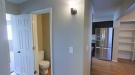 This multi-level residence spans three floors, offering a thoughtfully organized layout designed for comfortable everyday living. The interior showcases a neutral color palette with light gray and warm beige tones that create a clean, cohesive aesthetic throughout the home. Hardwood flooring adds warmth and continuity to the living areas, complementing the overall design scheme. The kitchen is equipped with modern stainless steel appliances, including a large French door refrigerator with an in-door ice and water dispenser, set against dark cabinetry that provides a striking contrast to the lighter walls. A convenient half bath is positioned just off the main corridor, featuring classic white fixtures and warm-toned walls. Wall-mounted sconce lighting adds a touch of character to the hallway, providing both functional illumination and a subtle decorative element. The thoughtful flow between spaces ensures easy navigation across all three levels, making the home well-suited for a variety of living arrangements. The combination of modern appliances, durable flooring, and a consistent neutral design language gives this residence a timeless and practical appeal.