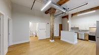 Located at 237-243 Furnace St in Akron, Ohio, this 2-bedroom, 1-bathroom unit masterfully blends historic industrial character with modern updates. The space showcases striking exposed red brick walls throughout, original timber beams, and soaring ceilings that lend an open, airy feel reflective of its converted building origins. Light wood-style flooring runs through the main living areas, adding warmth to the industrial aesthetic. The kitchen is a standout feature, highlighted by a dramatic full-height exposed brick wall with an arched window detail that floods the room with natural light. It is equipped with stainless steel appliances, a stainless range, a built-in microwave, ample cabinetry, and generous counter space. The two bedrooms offer comfortable accommodations, with plush carpeting, high ceilings, and closet storage. The primary bedroom features its own arched brick window, continuing the building's historic charm. The bathroom is designed with accessibility in mind, outfitted with grab bars, a roll-in tile shower, wall-mounted sink, and wood-look flooring. A washer is also conveniently located within the unit. This thoughtfully updated space captures the character of Akron's industrial heritage while delivering modern comfort and functionality.