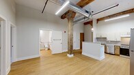 Located at 237-243 Furnace St in Akron, Ohio, this 2-bedroom, 1-bathroom unit masterfully blends historic industrial character with modern updates. The space showcases striking exposed red brick walls throughout, original timber beams, and soaring ceilings that lend an open, airy feel reflective of its converted building origins. Light wood-style flooring runs through the main living areas, adding warmth to the industrial aesthetic. The kitchen is a standout feature, highlighted by a dramatic full-height exposed brick wall with an arched window detail that floods the room with natural light. It is equipped with stainless steel appliances, a stainless range, a built-in microwave, ample cabinetry, and generous counter space. The two bedrooms offer comfortable accommodations, with plush carpeting, high ceilings, and closet storage. The primary bedroom features its own arched brick window, continuing the building's historic charm. The bathroom is designed with accessibility in mind, outfitted with grab bars, a roll-in tile shower, wall-mounted sink, and wood-look flooring. A washer is also conveniently located within the unit. This thoughtfully updated space captures the character of Akron's industrial heritage while delivering modern comfort and functionality.