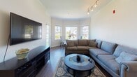 Located at 21 Dexter Road in Foxboro, Massachusetts, this single-floor residence offers a thoughtfully designed layout with a cohesive blend of modern finishes and comfortable living spaces. The open floor plan, visible in the 3D overview, connects key living areas in a functional and accessible arrangement.

The living room is a standout space, highlighted by a striking bay window configuration that frames neighborhood views and fills the room with natural light. Crown molding, track lighting, and dark hardwood-style flooring lend a polished character to the area, creating an inviting gathering space.

The kitchen is well-equipped with white shaker cabinetry, granite countertops, stainless steel appliances, and a peninsula with pendant lighting overhead. A walk-in pantry provides generous storage. The hardwood-style flooring continues seamlessly from the living areas into the kitchen.

The bedrooms feature plush carpeting and ample closet space, with bifold doors revealing well-organized storage. Natural light enters through sizeable windows offering views of the surrounding neighborhood.

Two bathrooms serve the residence. One features a white vanity with a granite top, an oval mirror, and light tile flooring. The second offers a shower with a curtain enclosure and matching tile flooring, maintaining the clean, neutral aesthetic found throughout the home.