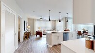 Located at 550 Stanton in Frederick, Maryland, this well-appointed 2-bedroom, 2-bathroom residence offers a thoughtfully designed open-concept layout across a single floor. The kitchen is a standout centerpiece, featuring white shaker cabinetry with glass-front uppers, a gray subway tile backsplash, stainless steel appliances, and a large island with a built-in sink and bar seating — all illuminated by dramatic black pendant lighting. The kitchen flows seamlessly into the dining area, which benefits from large windows and direct access to an exterior door, and further into the living room, where oversized windows, sheer drapery, and a ceiling fan create a bright, airy atmosphere. Wood-look flooring runs throughout the entire home, lending warmth and continuity. The primary bedroom is a comfortable retreat with a large window and direct access to an en-suite bathroom, which includes a white vanity, walk-in glass shower with subway tile, and a connected closet. The second bedroom offers similar natural light and easy access to a full second bathroom featuring a tub-shower combo with subway tile and a matching white vanity. Clean neutral tones and modern finishes define the overall aesthetic of this residence.