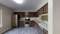 This single-floor residence offers a thoughtfully designed layout with modern finishes throughout. The kitchen is a standout feature, outfitted with rich dark-stained cabinetry, light stone-look countertops, and a full suite of stainless steel appliances including a refrigerator, electric range, over-the-range microwave, and dishwasher. Wood-look vinyl plank flooring ties the kitchen together, providing both durability and style. A pass-through window connects the kitchen to the living area, enhancing the open feel of the space. The living room is generously sized, featuring plush neutral carpeting, a tile-surround fireplace, and a large sliding glass door that floods the room with natural light and provides views of the surrounding greenery. The bedrooms are well-proportioned with soft carpeting, sliding windows with outdoor views, and ample closet space, including a walk-in closet with built-in shelving. The bathrooms are finished with dark wood vanities, light countertops, large mirrors, and wood-look vinyl flooring, maintaining a consistent design aesthetic throughout the home. Overall, the space presents a clean, contemporary look with a warm and comfortable ambiance.