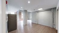 This single-floor unit blends industrial character with modern finishes throughout its efficiently arranged layout. Exposed brick walls—some left in their natural red tone, others painted white—are a defining architectural feature, lending a loft-like aesthetic to the space. Light wood-look flooring runs continuously throughout, unifying the open areas and complementing the unit's clean, contemporary palette.

The main open area is anchored by a structural column and benefits from multiple windows that draw in natural light. One window frames a notable waterfront view, offering a scenic outlook over a river and surrounding landscape. Recessed lighting and a skylight-style ceiling fixture supplement the natural light.

The kitchen is well-appointed with light wood cabinetry, white countertops, and a full suite of stainless steel appliances including a refrigerator, range, microwave, and dishwasher. A stainless steel sink with a modern faucet completes the functional workspace, set against a soft blue-gray accent wall.

The bathroom is finished in a clean, minimal style with wood-toned cabinetry, a white countertop vanity, a mirror, and wood-look flooring. Exposed conduit runs along several walls, reinforcing the unit's industrial character while maintaining a polished overall finish.