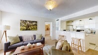 This single-floor residence offers a thoughtfully laid-out living space with a warm and inviting ambiance throughout. The living room is bright and comfortable, featuring plush carpeting, a textured ceiling with a classic flush-mount light fixture, and large sliding glass doors that open directly to a private outdoor patio, filling the space with natural light and providing easy access to the outdoors. A window alongside the sliding doors further enhances the airy feel of the room.

The kitchen is designed for functionality, featuring white cabinetry, tile flooring, and a suite of white appliances including a refrigerator, range, and microwave. A raised breakfast bar connects the kitchen to the living area, offering a convenient casual dining option and a sense of openness between the two spaces.

The bedrooms are cozy and well-sized, each finished with soft carpeting, ceiling fans, and windows dressed with patterned curtains that allow for natural light. The layout also includes access to a tiled bathroom from the bedroom area, complete with a single-sink vanity with ample cabinet storage and a full bathtub with shower.

A second bathroom, also finished in tile with a clean white vanity and large mirror, serves the remainder of the unit. The overall design is clean, neutral, and functional, offering a comfortable and practical living environment.