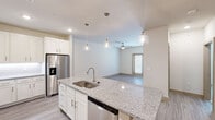 This one-bedroom, one-bathroom residence in Grand Prairie, TX is thoughtfully designed to maximize functionality within a well-proportioned single-story layout. The open-concept kitchen and living area serves as the heart of the home, anchored by a central island with granite countertops, an undermount sink, and pendant lighting overhead. White shaker-style cabinetry lines the kitchen walls, complemented by a white subway tile backsplash and a full suite of stainless steel appliances, including a French door refrigerator, electric range, microwave, and dishwasher. Light wood-look flooring flows throughout the main living areas, enhancing the bright, airy atmosphere. The living room features a ceiling fan and double French doors that allow natural light to fill the space. The bedroom is carpeted for comfort, includes a ceiling fan, and offers access to a walk-in closet equipped with double hanging rods and shelving. The bathroom presents a double-sink vanity with granite countertops, white cabinetry, and a large mirror with overhead lighting. Neutral tones and clean finishes throughout contribute to a cohesive, modern aesthetic.