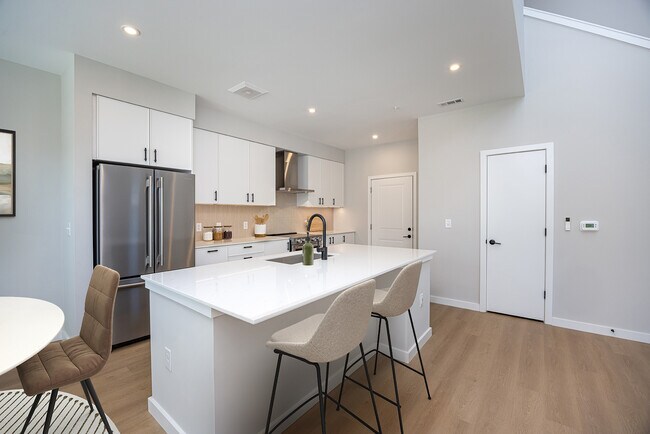 Cocina de la colección Upgrade 3BR Townhome con gabinetes blancos, encimeras de cuarzo blanco y campana extractora sobre la estufa. - Avalon Brier Creek