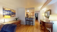Located on N La Salle Drive in Chicago's prestigious Gold Coast neighborhood, this single-floor residence offers a warm and cohesive living experience throughout its well-designed layout. Gleaming hardwood floors run continuously through the main living areas, lending a sense of warmth and continuity to the space.

The living room is a standout feature, anchored by a graceful curved bay window that fills the room with natural light. Generous seating, a central coffee table, and thoughtful wall art create an inviting and comfortable atmosphere. Adjacent to the living area, a dedicated entertainment nook provides additional functional space.

The kitchen is efficiently designed with light maple cabinetry, granite countertops, and stainless steel appliances including a gas range and built-in microwave. A breakfast bar with bar seating connects the kitchen to the dining area, making it ideal for casual meals and entertaining. The dining space comfortably accommodates a full table and chairs.

The bedroom is a tranquil retreat, featuring hardwood floors, a window with drapery, a large tufted upholstered headboard, and a mirrored closet that enhances the sense of space. The bathroom is elegantly appointed with a glass-enclosed walk-in shower featuring marble-style tile surround, a mosaic tile floor, and modern wood-toned vanity cabinetry.