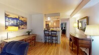 Located on N La Salle Drive in Chicago's prestigious Gold Coast neighborhood, this single-floor residence offers a warm and cohesive living experience throughout its well-designed layout. Gleaming hardwood floors run continuously through the main living areas, lending a sense of warmth and continuity to the space.

The living room is a standout feature, anchored by a graceful curved bay window that fills the room with natural light. Generous seating, a central coffee table, and thoughtful wall art create an inviting and comfortable atmosphere. Adjacent to the living area, a dedicated entertainment nook provides additional functional space.

The kitchen is efficiently designed with light maple cabinetry, granite countertops, and stainless steel appliances including a gas range and built-in microwave. A breakfast bar with bar seating connects the kitchen to the dining area, making it ideal for casual meals and entertaining. The dining space comfortably accommodates a full table and chairs.

The bedroom is a tranquil retreat, featuring hardwood floors, a window with drapery, a large tufted upholstered headboard, and a mirrored closet that enhances the sense of space. The bathroom is elegantly appointed with a glass-enclosed walk-in shower featuring marble-style tile surround, a mosaic tile floor, and modern wood-toned vanity cabinetry.