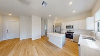 This contemporary single-floor residence showcases a clean, modern design throughout, highlighted by light hardwood flooring that runs seamlessly across every room. The open-concept layout connects the kitchen and living area into a cohesive, airy space filled with natural light. The well-appointed kitchen features a central island with a white quartz countertop, a full suite of stainless steel appliances including a French door refrigerator with ice and water dispenser, electric range, built-in microwave, and dishwasher. Cabinetry combines crisp white upper cabinets with warm wood-toned lower cabinets, providing ample storage. Recessed lighting and a window above the sink add both function and brightness. The living area opens directly to a private outdoor patio through a large sliding glass door dressed with vertical blinds, inviting natural light and outdoor views. The bedrooms are generously proportioned, each offering closet storage and large windows that allow natural light to filter in. The bathroom is finished with a full tub-shower combination, a vanity with quartz countertop, and clean white fixtures. Throughout, the neutral color palette and modern architectural details create a bright, welcoming atmosphere.