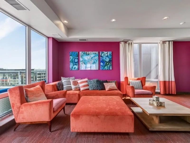Modern living room with orange sectional sofa, accent chairs, and pink walls.