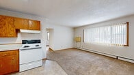 Located at 1209 20th St S in Moorhead, Minnesota, this unit offers a practical and well-organized single-floor layout comprising three bedrooms, one bathroom, a living room, kitchen, and hallway. The living room is a comfortable, open space featuring neutral carpet flooring, a large window with vertical blinds that allows generous natural light, and a baseboard heating unit. It connects seamlessly to the kitchen, which is finished with tile flooring and outfitted with warm oak cabinetry, white appliances including an electric range and refrigerator, a built-in sink, and a flush-mounted ceiling light. Each of the three bedrooms is carpeted and features windows with blinds that invite natural light. Several bedrooms include built-in closets with wood-panel sliding or hinged doors, providing practical storage. The bathroom features tile flooring, a wall-mounted sink, a vanity mirror with overhead lighting, and a shower-tub combination. Throughout the unit, light-toned wood trim and neutral walls create a clean, consistent aesthetic. Textured ceilings and baseboard heating are present in multiple rooms. The overall layout is efficient and straightforward, making the most of the available space.