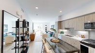 This well-designed 2-bedroom, 1-bathroom residence offers a thoughtful single-level layout that maximizes every square foot. The open-plan living and kitchen area serves as the heart of the home, featuring light wood-look flooring, recessed lighting, and a bright, airy ambiance created by white walls and a clean, modern aesthetic. The kitchen is fully equipped with flat-front cabinetry in a warm wood tone, a subway-tile backsplash, white quartz countertops, stainless steel appliances including a gas range, dishwasher, and French door refrigerator, and a sleek undermount sink. A compact dining area with a glass-top table and bar seating flows seamlessly from the kitchen. The living room provides comfortable space for lounging and opens toward a private balcony, allowing natural light to filter through. The primary bedroom accommodates a queen-sized bed comfortably and includes a built-in closet with sliding frosted-panel doors and a window with outdoor views. The second bedroom is similarly sized with its own window. The bathroom features a soaking tub with a full marble-look tile surround, a built-in niche, and a curved shower rod. A hallway connects all rooms efficiently, completing this cohesive and contemporary residence.