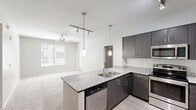 This 2-bedroom, 2-bathroom residence in Phoenix, AZ offers a clean, contemporary design across a single, efficiently organized floor. The open-concept kitchen is a standout feature, equipped with dark espresso cabinetry, granite-style countertops, stainless steel appliances including a refrigerator, range, microwave, and dishwasher, and a central island with a double sink illuminated by pendant lighting. Track lighting and a seamless transition to light wood-style flooring complete the kitchen's modern aesthetic. The living area extends from the kitchen and features plush carpeting and a ceiling fan, with natural light flowing in through large windows with blinds. Both bedrooms are carpeted and spacious, each featuring ceiling fans and windows that bring in natural light and exterior views. The primary bedroom offers a comfortable, well-proportioned retreat. Both bathrooms are finished with light wood-style flooring, white tub-shower combinations, and brushed nickel fixtures; one bathroom also includes a dark-cabineted vanity with a granite-style countertop. A hallway leads through the space, which also includes an in-unit stacked washer and dryer closet accessible from the entryway — a highly practical convenience.