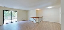 This well-appointed single-floor unit features a clean, neutral aesthetic throughout, with warm hardwood-style flooring extending across the main living areas and bedrooms. The open living room is a standout space, offering generous square footage, soft natural light, and direct access to a private balcony through a full-length sliding glass door. The balcony overlooks lush, mature tree coverage, providing a tranquil outdoor connection. A staircase with a distinctive wood-and-iron railing adds architectural interest and connects to the lower level.

The galley-style kitchen is efficiently designed, featuring warm wood cabinetry, white countertops, a gas range, and a sink, all set on light-toned tile flooring. Multiple bedrooms are spread throughout the unit, each benefiting from windows with leafy outdoor views and consistent hardwood-style flooring. The bedrooms include closet access, providing practical storage solutions.

The bathroom is finished with light tile flooring, a wood-toned vanity with an integrated sink, a full soaking tub, and a window that brings in natural light. Throughout the space, the neutral cream-toned walls and consistent finishes create a cohesive, understated ambiance suited to a variety of interior styles.