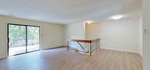 This well-appointed single-floor unit features a clean, neutral aesthetic throughout, with warm hardwood-style flooring extending across the main living areas and bedrooms. The open living room is a standout space, offering generous square footage, soft natural light, and direct access to a private balcony through a full-length sliding glass door. The balcony overlooks lush, mature tree coverage, providing a tranquil outdoor connection. A staircase with a distinctive wood-and-iron railing adds architectural interest and connects to the lower level.

The galley-style kitchen is efficiently designed, featuring warm wood cabinetry, white countertops, a gas range, and a sink, all set on light-toned tile flooring. Multiple bedrooms are spread throughout the unit, each benefiting from windows with leafy outdoor views and consistent hardwood-style flooring. The bedrooms include closet access, providing practical storage solutions.

The bathroom is finished with light tile flooring, a wood-toned vanity with an integrated sink, a full soaking tub, and a window that brings in natural light. Throughout the space, the neutral cream-toned walls and consistent finishes create a cohesive, understated ambiance suited to a variety of interior styles.
