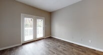 This 1-bedroom, 1-bathroom single-story unit offers a practical and comfortable layout with consistent neutral tones and durable finishes throughout. The living area features wood-look hardwood-style flooring and is filled with natural light courtesy of a set of glass French doors that open directly to a private outdoor balcony or patio, making the space feel open and connected to the outdoors. The kitchen is efficiently designed with ample white cabinetry, a granite-style countertop, a coil-top range, and a single-basin sink — all illuminated by a track lighting fixture overhead. Adjacent to the kitchen, a dedicated entry area provides easy access in and out of the unit. The bedroom is a quiet retreat with plush wall-to-wall carpet, a window with a view of surrounding greenery, and a louvered closet door offering generous storage. Closet space is further supplemented by an additional built-in storage closet visible in the hallway area. The bathroom is clean and well-appointed, featuring a tub-shower combo with white tile surround, a toilet, and a vanity with a granite-look countertop. Textured ceilings are consistent throughout the unit, adding a classic residential feel to the overall design.