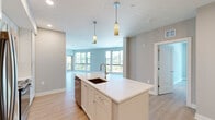 This contemporary 2-bedroom, 2-bathroom unit offers a well-designed single-level layout with clean finishes and a bright, modern aesthetic. The open-concept kitchen and living area serves as the heart of the unit, anchored by a generously sized center island with a crisp white quartz countertop, an undermount sink, and stylish pendant lighting above. The kitchen is equipped with stainless steel appliances, including a refrigerator, range, and microwave, complemented by white shaker-style cabinetry and a classic subway tile backsplash. Light-toned hardwood flooring flows seamlessly throughout the entire unit, enhancing the sense of openness. The living area is bathed in natural light from an expansive bank of windows, offering views of the surrounding neighborhood. Both bedrooms are comfortably proportioned with neutral wall tones and ample closet storage, including a dedicated closet in the secondary bedroom. The two bathrooms are finished with marble-style tile flooring and white subway tile surrounds. One bathroom features a full soaking tub and shower combination, while the other includes a well-appointed vanity with a large mirror. The unit also includes a dedicated closet for additional storage.
